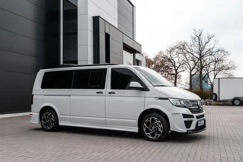 A white van parked on a paved forecourt outside a modern dark grey building.